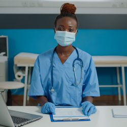 Portrait of medical nurse looking at camera with face mask while sitting at desk in checkup cabinet. Young woman working as assistant wearing uniform and gloves for virus protection SSUCv3H4sIAAAAAAAACpRSy27cMAy8F+g/GDpHqK2HHeULcgnQe9EDJdO7QrTWQpJTFEH+vfQr1aWHHmyYQ3I4Q/P965emYRayd+ypeV8jin0ISy4Jio8zwe3DgSecR0w18pZk39YAjr7E5CHUoIXirjPckMB5CWGFP7YkywXKkjGv0w/IQcELcezgJ8Uu8cceN2diS1IHpdgzQihXBwm/vZAORyIeqqq82LXqxWeHIcCMccnszO+z/0H8HeM94H+Q7R8/T/9wwdn93ixW1hMGhN364Yo9Gjlp5XpuYVRcdZPmQG8uOjGYwdp+UMMpg4HUTuth4u1gDFc9dRhQjrcTqk4YI/X4t7ibHNheImVty5UQkmYoxXthLUornTDdpn8XzV5/FUy3+rfAMvpY/ZG3SAteC2Tl6Z688/Olaovlup3M2ebiMpe0LoN9igsx3sHShp+aiTjxxK+QM5WPJ14NcnSg8VbNmWPZVnmwspGuaA07KQbZ9lr0otWPtBh9FOyXd/XEs8k5iSh2r36srftVAdPKTpIeLpTtuBqF4UaIlmtj9WidnFADrfDjDwAAAP//AwAs+XBOVAMAAA==